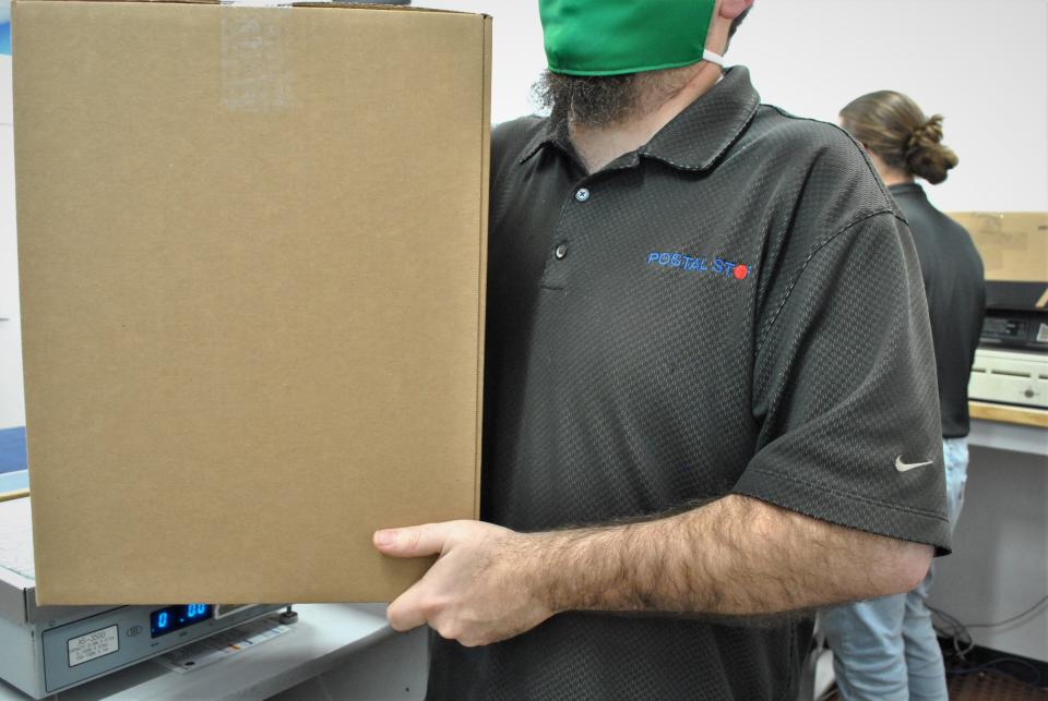 Cameron Wells, owner of the Postal Stop in west Eugene, carries a box labeled for shipping.