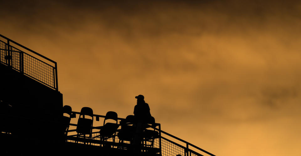 A lone fan stands in the upper deck of Coors Field as the sun sets in the fifth inning of a baseball game between the Chicago White Sox and the Colorado Rockies, Friday, Aug. 18, 2023, in Denver. (AP Photo/David Zalubowski)