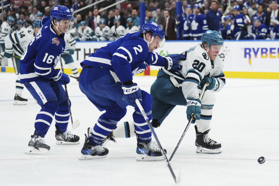 Toronto Maple Leafs defenseman Simon Benoit (2) checks San Jose Sharks forward Fabian Zetterlund (20) as Maple Leafs forward Mitchell Marner (16) looks on during the third period of an NHL hockey game, Tuesday, Jan. 9, 2024 in Toronto. (Nathan Denette/The Canadian Press via AP)