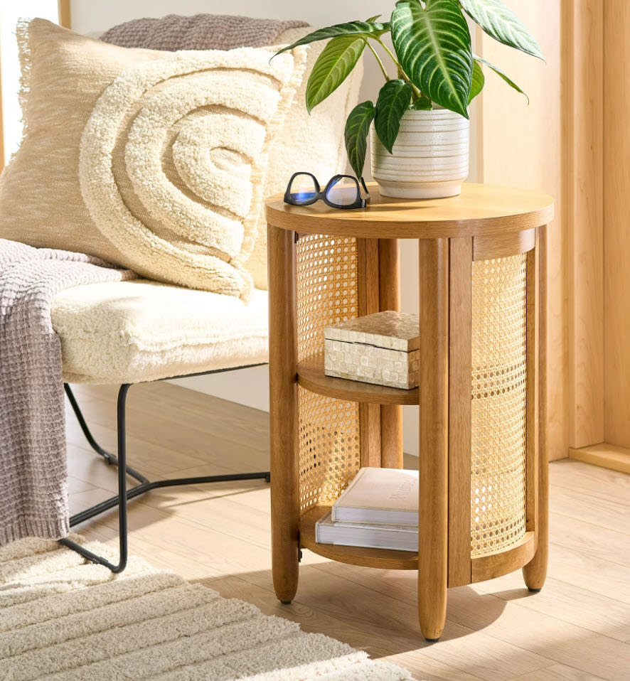 Side table with books, a plant, glasses, and a decorative pillow in a cozy room setting