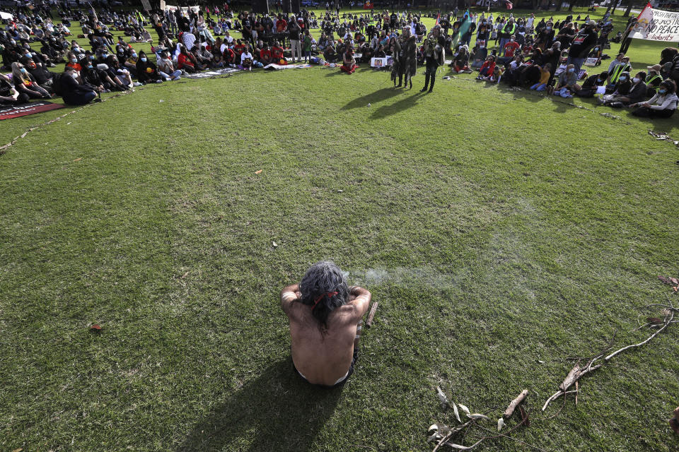 An Aboriginal man sits with a small fire during a traditional smoking ceremony as thousands gather at a rally supporting the Black Lives Matter and Black Deaths in Custody movements in Sydney, Sunday, July 5, 2020. (AP Photo/Rick Rycroft)