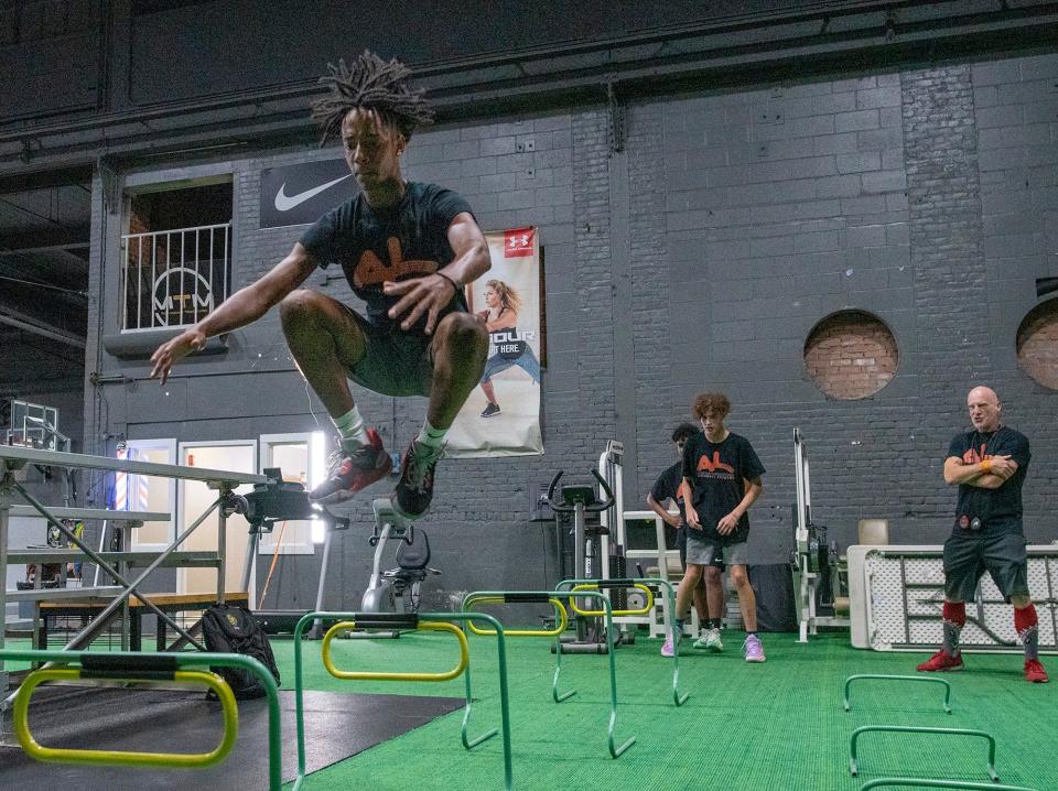 Ian Johnson leaps over hurdles at a conditioning station led by trainer Paul Reynolds, far right, during the Back to School Camp at McClain’s Training Method last Friday.