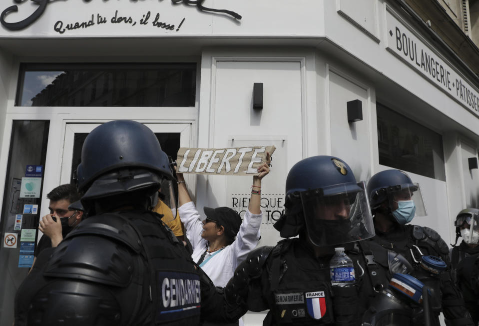 A protestor holds up a banner which reads "freedom" as she stands between police during a demonstration in Paris, France, Saturday, July 31, 2021. Demonstrators gathered in several cities in France on Saturday to protest against the COVID-19 pass, which grants vaccinated individuals greater ease of access to venues. (AP Photo/Adrienne Surprenant)