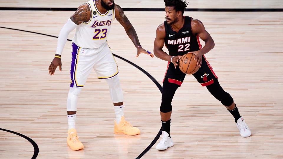 lebron james, wearing a white los angeles lakers jersey, covers jimmy butler, wearing a black miami heat jersey, on a basketball court