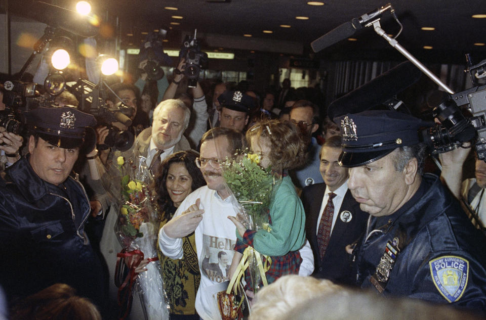 FILE - Former hostage Terry Anderson, center, carries his daughter Sulome, 6, through a crunch of media upon arrival to John F. Kennedy International Airport in New York, Dec. 10, 1991. At left is Sulome's mother, Madeleine Bassil, and at immediate right is Associated Press President Lou Boccardi. Fellow former hostages, family, and coworkers celebrated the life of journalist and philanthropist Terry Anderson, Wednesday, May 8, 2024, as a man who helped others while struggling to heal himself. (AP Photo/Ed Bailey, File)