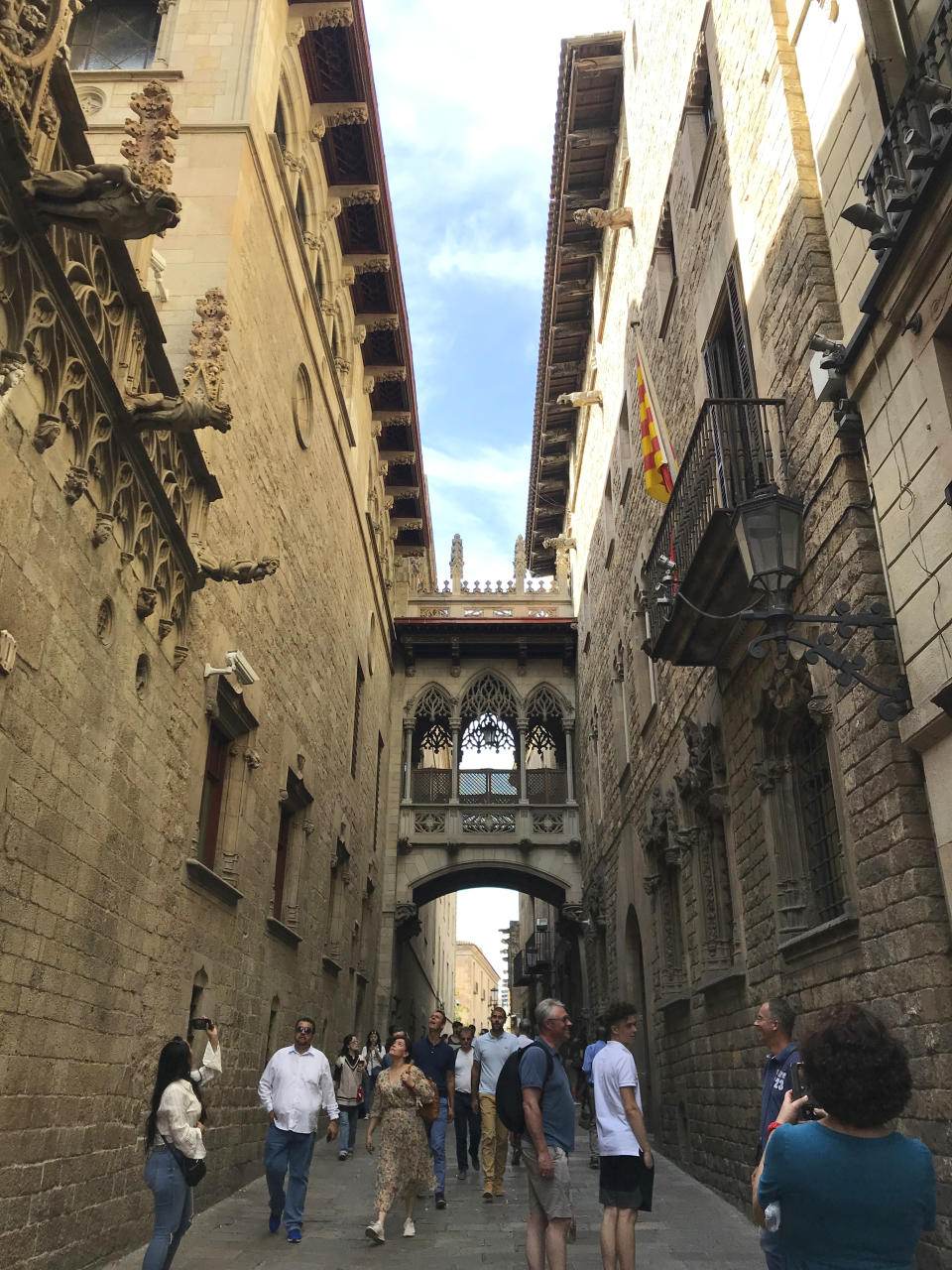 This Oct. 7, 2019 photo tourists walking along a narrow street between two old buildings in the Gothic Quarter of Barcelona, Spain. (Courtney Bonnell via AP)