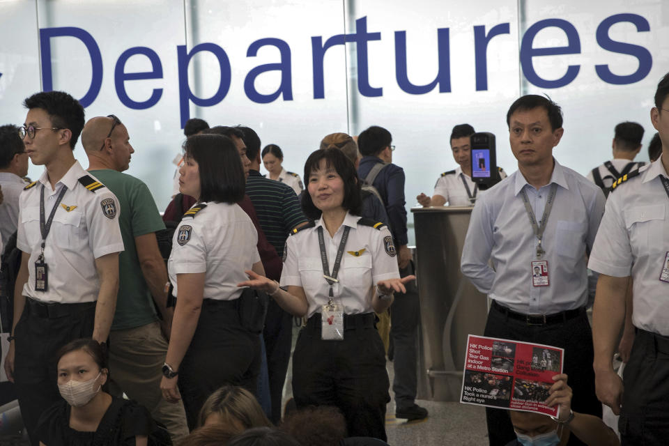 An airport security staff member gestures to travelers at the Hong Kong International Airport in Hong Kong, Tuesday, Aug. 13, 2019. Protesters clogged the departure area at Hong Kong's reopened airport Tuesday, a day after they forced one of the world's busiest transport hubs to shut down entirely amid their calls for an independent inquiry into alleged police abuse. (AP Photo/Vincent Thian)