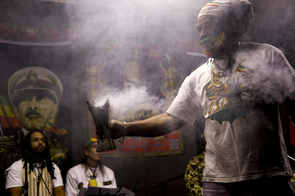 From left, Mosiyah Tafari and Binghi Neal take a break from traditional nyabinghi drumming and chanting on stage as frankincense wafts from a burner held by Ras Jahbo, center, during an event by the Rastafari Coalition marking the 91st anniversary of the coronation of the late Ethiopian Emperor Haile Selassie I in Columbus, Ohio on Tuesday, Nov. 2, 2021. As public opinion and policy continues to shift in the U.S. and across the world towards the use of marijuana, some adherents of Rastafari question their place in the future of the herb that they consider sacred. (AP Photo/Luis Andres Henao)