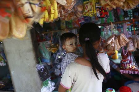 A woman holds a child as she shops for food at a shop in Kanhla village, an area to be included in the New City Project, outside Yangon August 30, 2014. REUTRS/Soe Zeya Tun