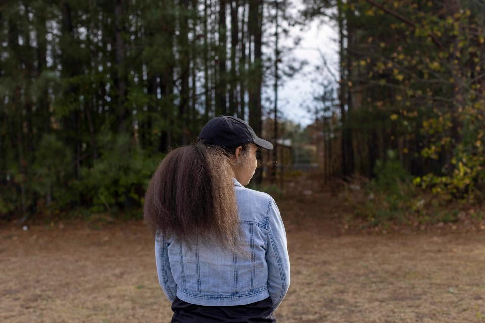 A woman stands in front of the woods by herself.