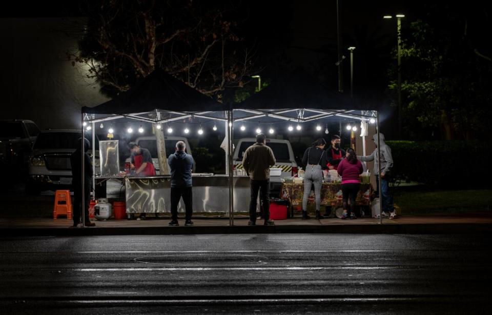 People stand under lighted tents at night.