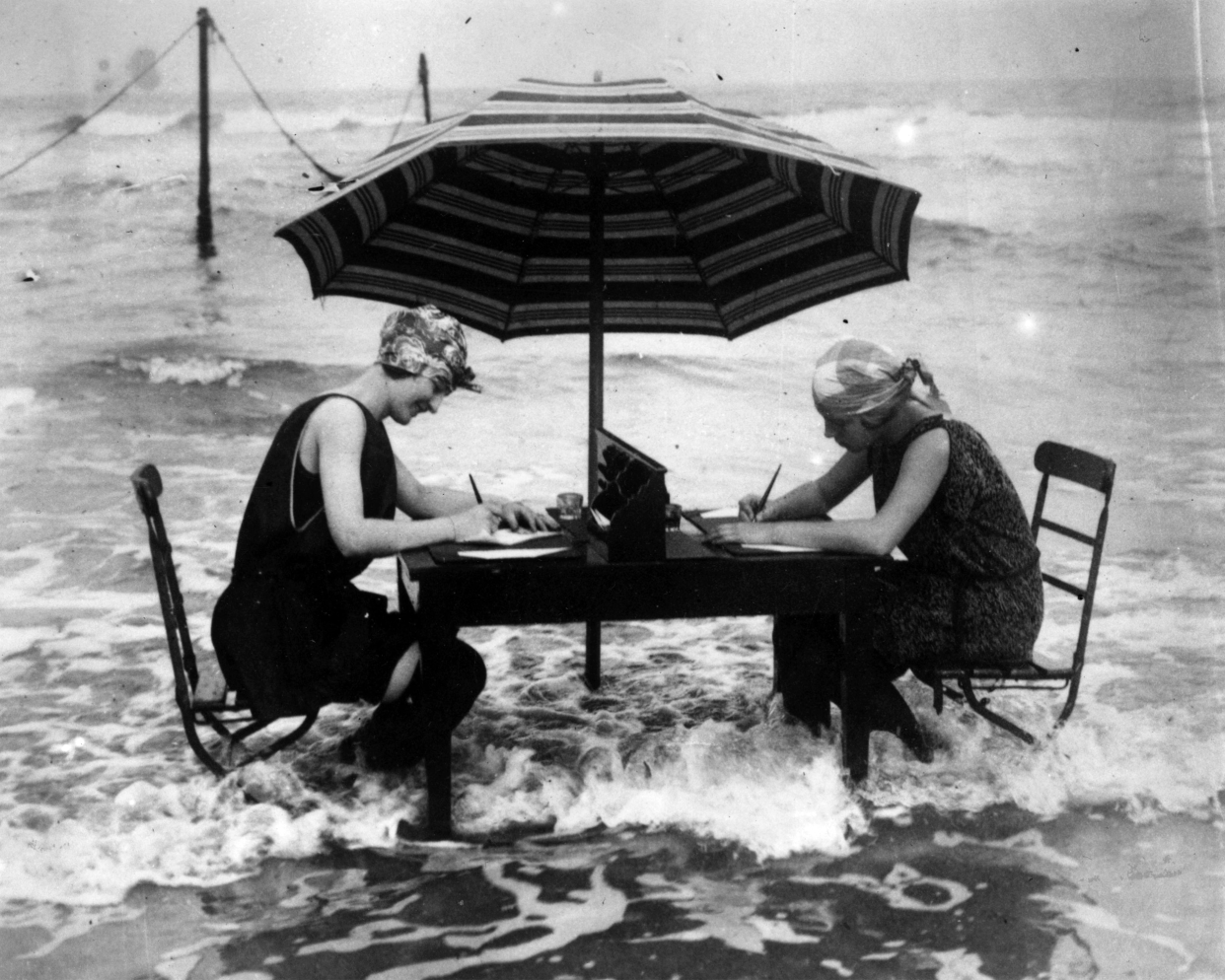 Two women brave the lapping waves at their feet as they continue with their correspondence at the water's edge