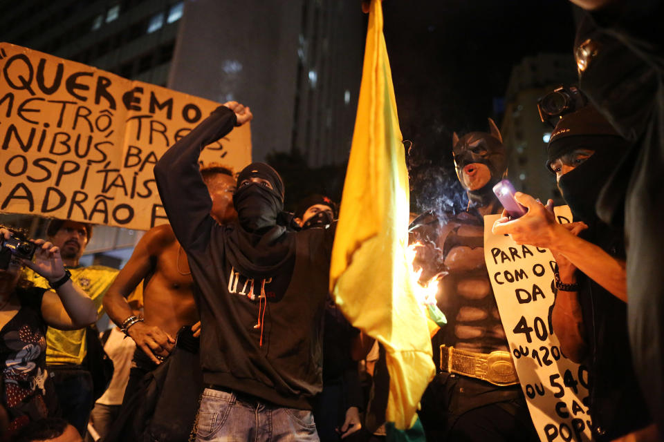 Masked demonstrators set fire to a jersey with the colors of Brazilian national soccer team during protest against the World Cup 2014, in Rio de Janeiro, Brazil, Thursday, March 27, 2014. Demonstrators call for better schools, health care, questioning the billions spent to host this year's World Cup and the 2016 Olympics. (AP Photo/Leo Correa)