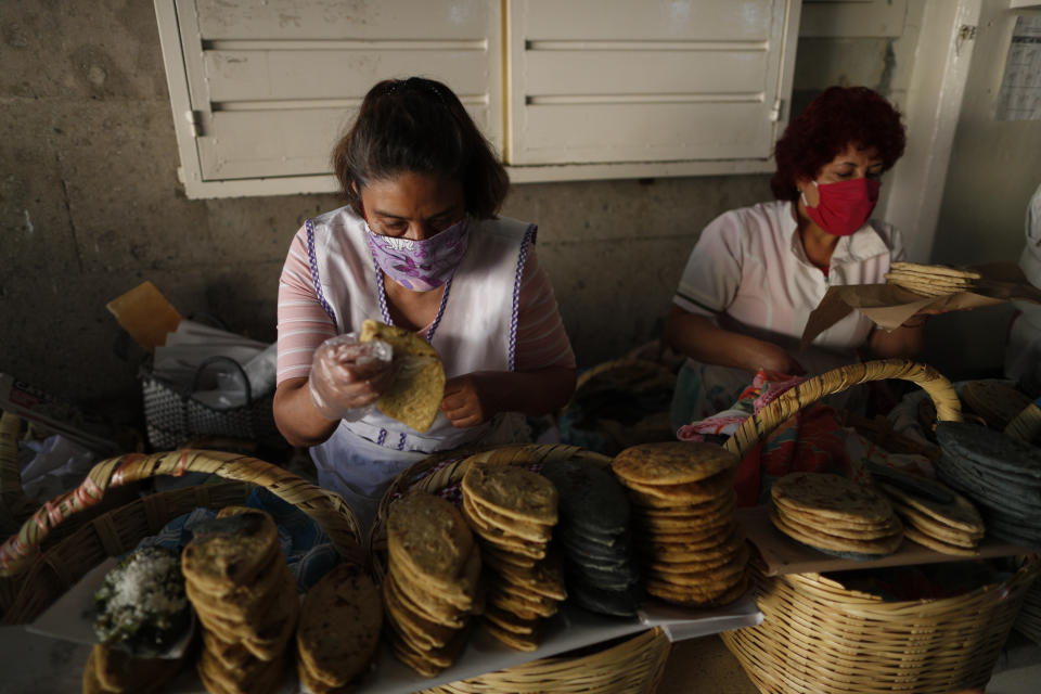 Hilda Trejo, left, and Sara Vargas Lopez wear face masks as they sell tlacoyos and sopes in a partially-open public market in the Xochimilco district of Mexico City, Friday, May 15, 2020. As Mexico moves toward a gradual reactivation of its economy Monday, the number of new coronavirus infections grows higher every day, raising fears of a new wave of infections that other countries have seen after loosening restrictions. (AP Photo/Rebecca Blackwell)