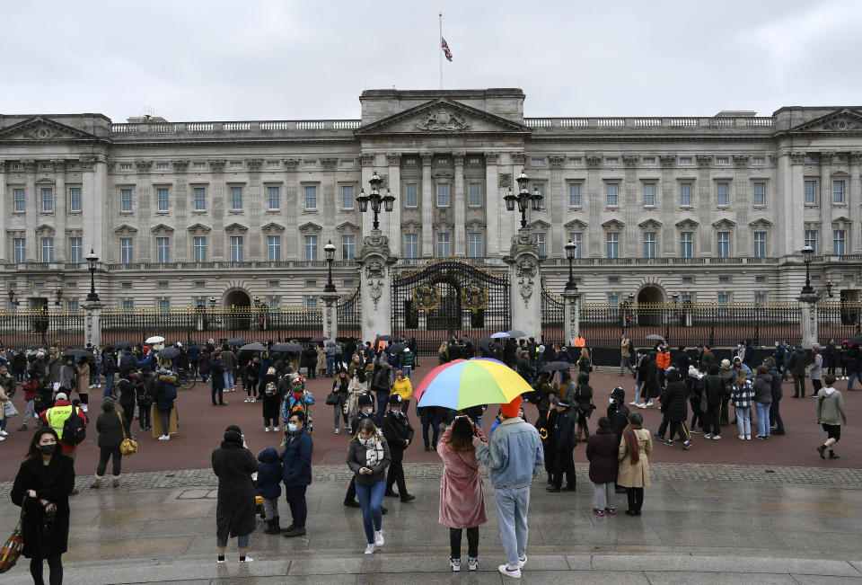 A couple under an umbrella gather with others outside the gates at Buckingham Palace in London, a day after the death of Britain's Prince Philip, Saturday, April 10, 2021. Britain's Prince Philip, the irascible and tough-minded husband of Queen Elizabeth II who spent more than seven decades supporting his wife in a role that mostly defined his life, died on Friday. (AP Photo/Alberto Pezzali)