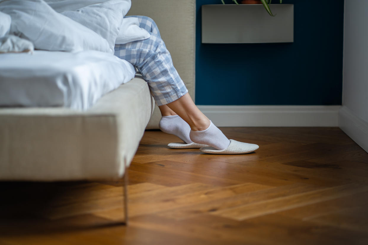 Woman relaxing at home in pyjamas and white socks sits on bed wearing comfortable slippers, casual lifestyle. Early rise, healthy sleeping, to start new day. Calm rested waking up in morning.