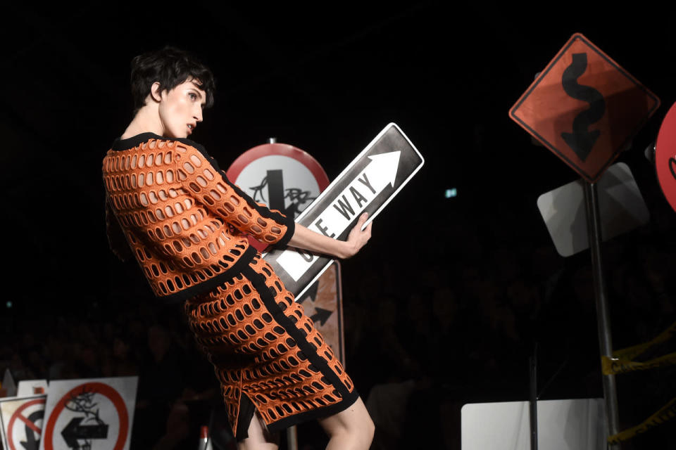 A model vamps with a “One Way” sign clutch on Moschino’s spring 2016 runway.