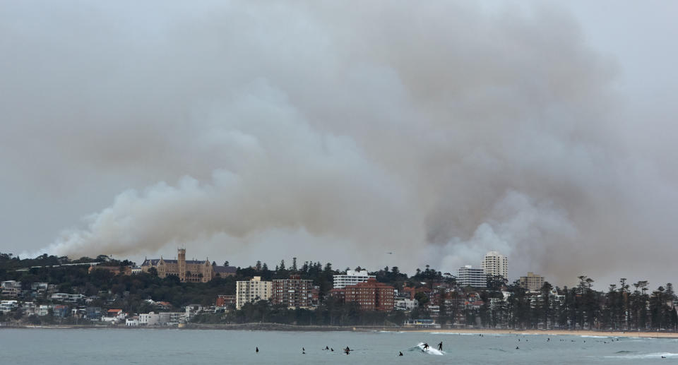 A photo of swimmers at a Sydney beach while there's smoke haze in the air from hazard reduction burning.