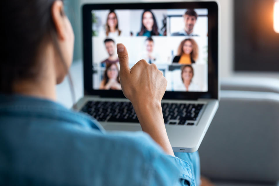 Back view of business woman making video call and showing thumb up to laptop on the online briefing while sit on sofa at home.