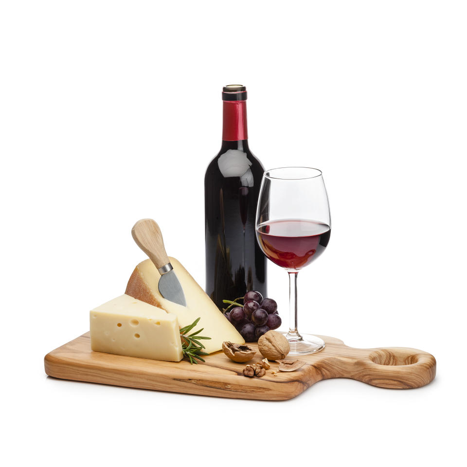 Cheese and wine: cutting board with cheese slices, grape and walnuts isolated on white background. A red wine bottle and a wineglass are behind the cheese tray. Useful copy space available for text and/or logo. High key DSRL studio photo taken with Canon EOS 5D Mk II and Canon EF 100mm f/2.8L Macro IS USM.