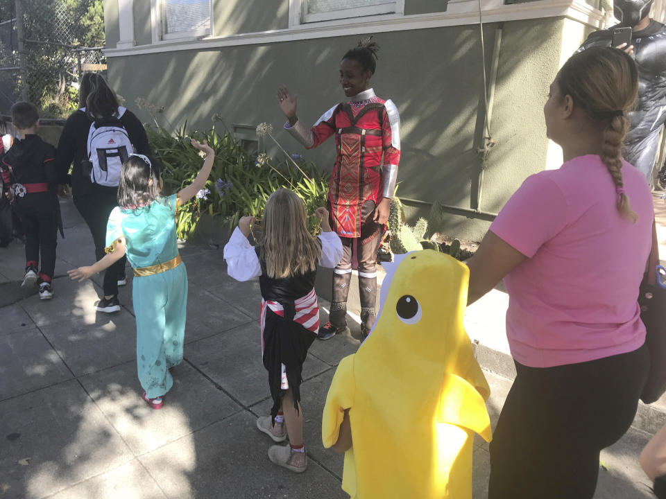 Berkeley Unified School District employee Nikkya Harris, dressed as Okoye from Black Panther, waves at students of Washington Elementary during their annual Halloween Parade on Thursday, Oct. 31, 2019, in Berkeley, Calif. The school had considered holding the parade indoors if the air quality was questionable because of a massive wildfire in Northern California's wine country. For tens of thousands of children in California, the biggest monsters this Halloween are wildfires that have thrown trick-or-treating into disarray. (AP Photo/Liz Schultz)