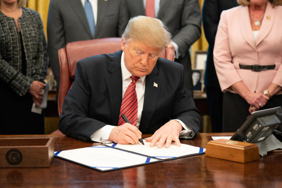 President Trump signing a bill at his desk in the Oval Office.