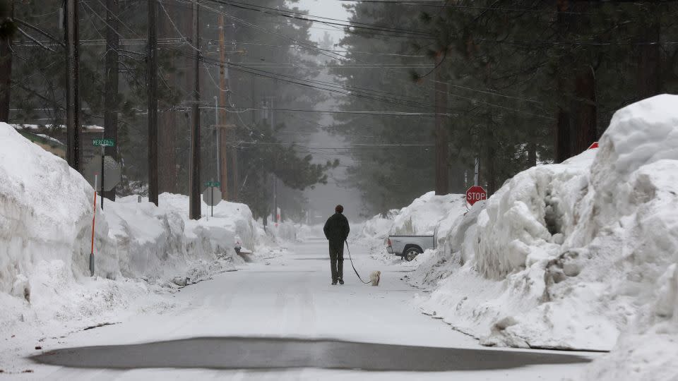 A man walks his dog on a snow covered street as snow begins to fall during an atmospheric river on March 21, 2023 in South Lake Tahoe, California. - Justin Sullivan/Getty Images