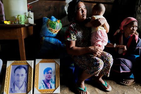 Women sit with a baby, son of one of their killed relatives next to pictures of victims Aik Lu (L) and Aik Sai after their bodies were found in a grave last June at Mong Yaw village in Lashio, Myanmar July 10, 2016. REUTERS/Soe Zeya Tun