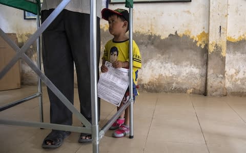 A boy watches his father vote as Cambodians cast their ballots during an election that has been criticised by the US and the EU - Credit: Paula Bronstein/Getty