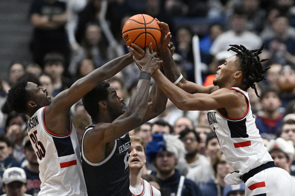 UConn forward Samson Johnson, left, Georgetown forward Supreme Cook, center, and UConn guard Stephon Castle, right, reach for the ball in the second half of an NCAA college basketball game, Sunday, Jan. 14, 2024, in Hartford, Conn. (AP Photo/Jessica Hill)