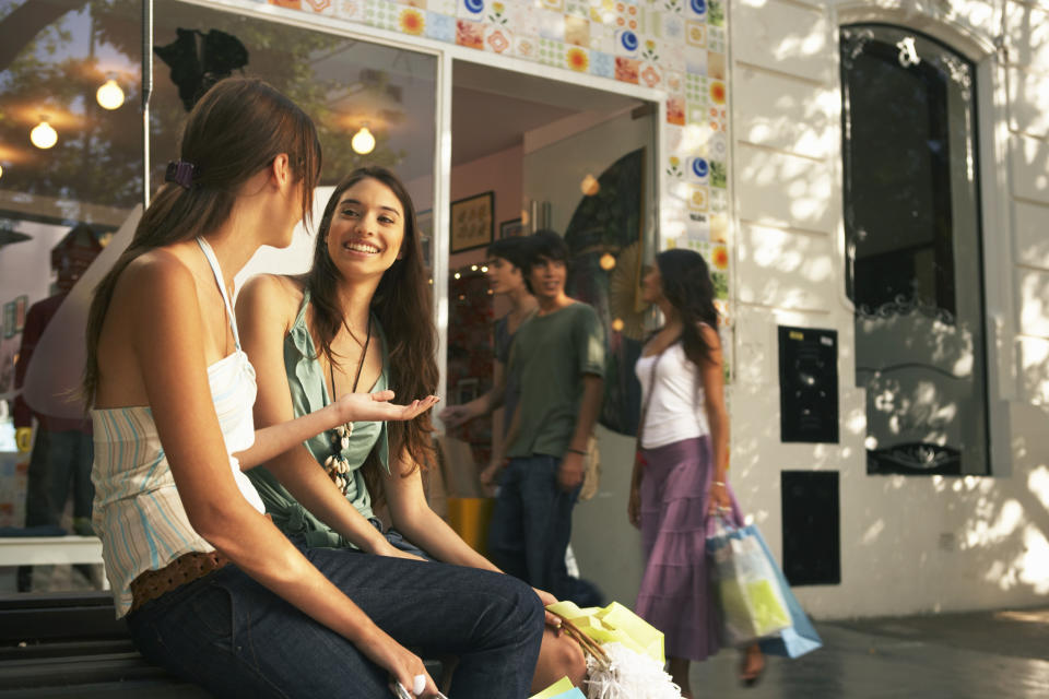 Two young women sitting outside a store.