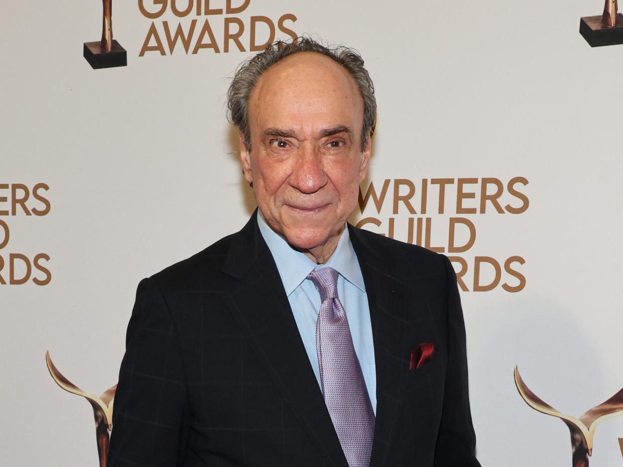 f. murray abraham, an 83-year-old man with a receding hairline, standing on a red carpet while wearing a black suit