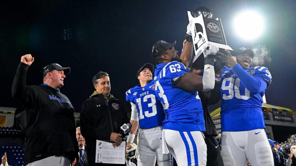 Duke offensive lineman Jacob Monk (63), defensive tackle DeWayne Carter (90) and quarterback Riley Leonard (13) hold the Military Bowl trophy as head coach Mike Elko, left, cheers after the Military Bowl NCAA college football game against UCF, Wednesday, Dec. 28, 2022, in Annapolis, Md. (AP Photo/Terrance Williams)
