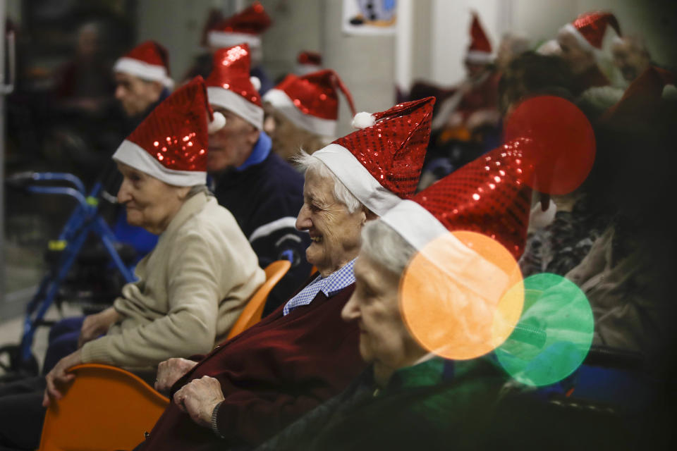 Hosts, protected by a glass window, attend a Christmas concert at the Martino Zanchi nursing home in Alzano Lombardo, one of the area that most suffered the first wave of COVID-19, northern Italy, Saturday, Dec. 19, 2020, as the hosts celebrate Christmas. (AP Photo/Luca Bruno)