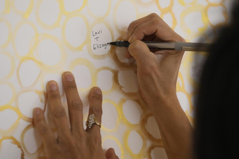 Michele Elizaga writes her dad's name on a grief project memorial to remember those who died from COVID-19 during a memorial event at the Arizona Heritage Center on March 6, 2023. Her dad died on Dec. 1, 2020.