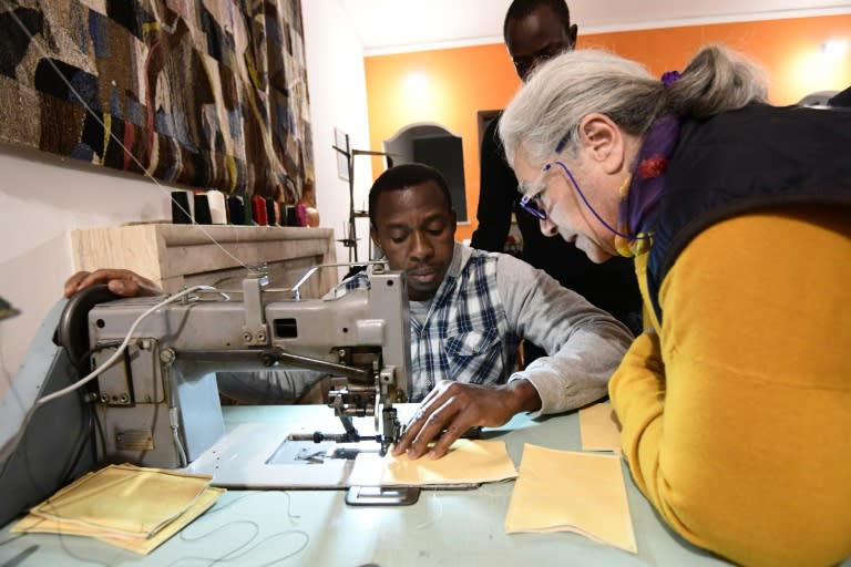 Issa, a migrant from Burkina Fasso, works at a sewing machine with the help of a volunteer at the training programme in leather bag making, one of 18 new participants