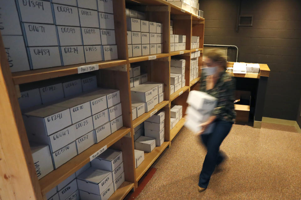 In this Tuesday, May 5, 2020, photo, Cook County Medical Examiner's Indigent Coordinator, Rebeca Perrone, begins placing 24 boxes of unclaimed cremated remains on a shelf, adding to over 500 other boxes at the county morgue in Chicago. Numbers of unclaimed remains are up, Perrone says. Lost wages amid business shutdowns mean some families can't afford the minimal $250 fee to collect the boxes. (AP Photo/Charles Rex Arbogast)