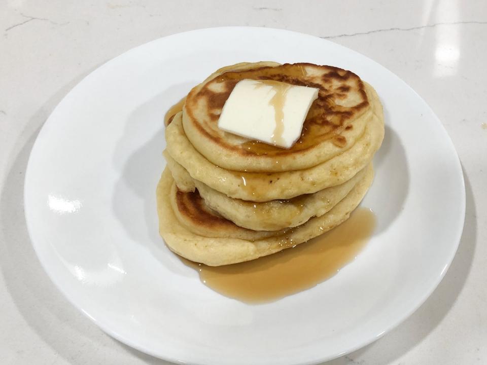 A stack of pancakes topped with butter and syrup on a white plate on the counter.