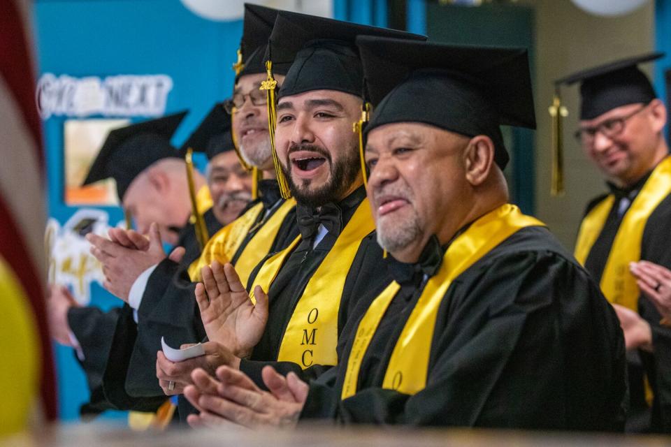 Men in camp, gown and a yellow sash smile, clap and cheer