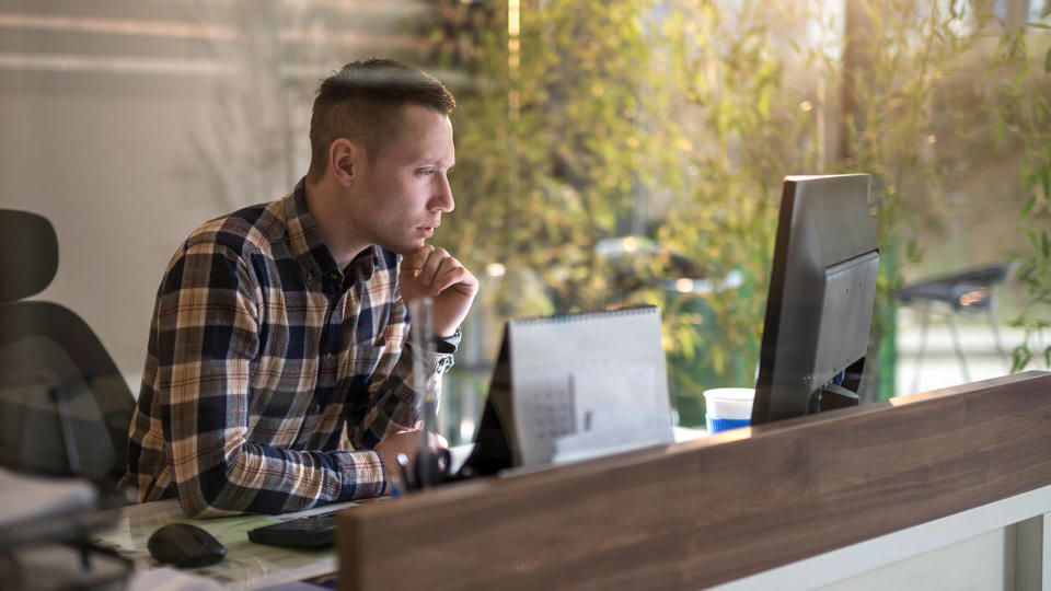 Young pensive businessman holding hand on chin and looking at desktop PC in the office.