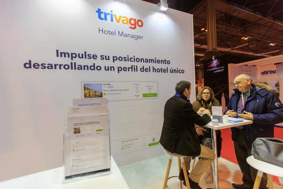 Three people at a table talking at an industry conference next to a sign for Trivago's hotel manager.