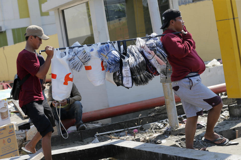 In this Sunday, Sept. 30, 2018, file photo, workers carry goods from their shop at a shopping mall damaged by a massive earthquake and a tsunami in Palu, Central Sulawesi, Indonesia. (AP Photo/Tatan Syuflana, File)