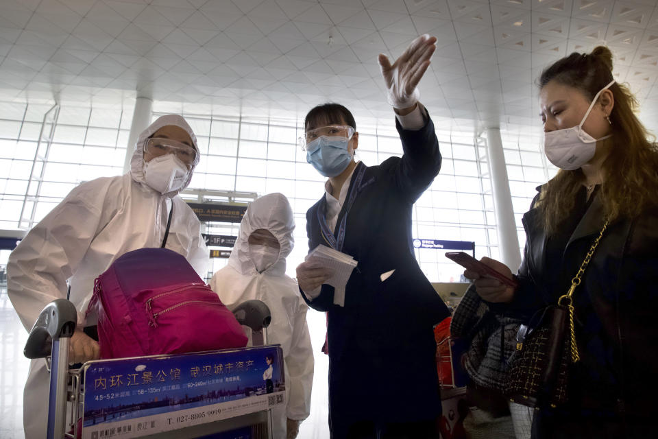 A worker directs travellers wearing face masks and suits to protect against the spread of new coronavirus at Wuhan Tianhe International Airport (Ng Han Guan/AP)