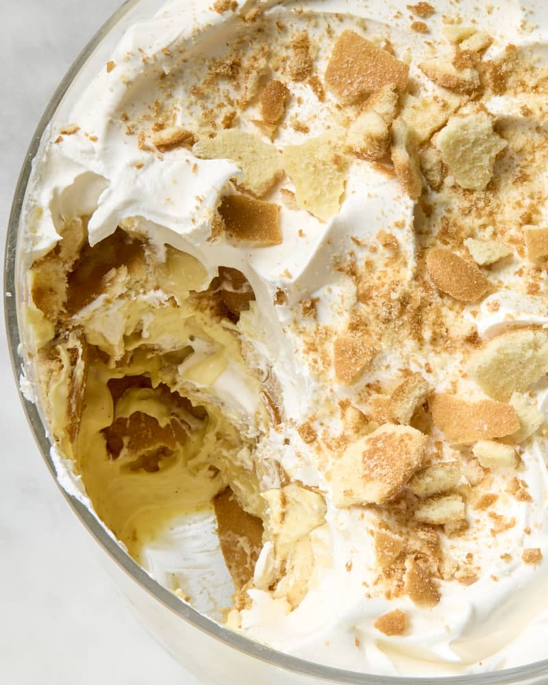 overhead shot of banana pudding topped with nilla wafers in a trifle dish, with a large scoop taken out of the left side.