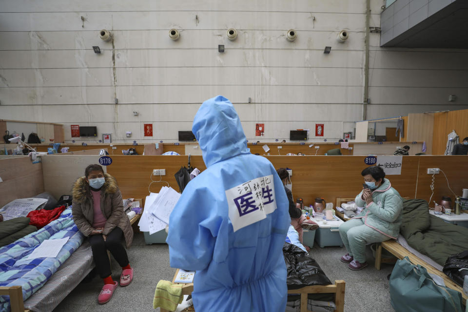 In this Friday, Feb. 21, 2020, photo, a doctor in a protective suit checks with patients at a temporary hospital at Tazihu Gymnasium in Wuhan in central China's Hubei province. China's leadership sounded a cautious note Friday about the country's progress in halting the spread of the new virus that has now killed more than 2,200 people, after several days of upbeat messages. (Chinatopix via AP)