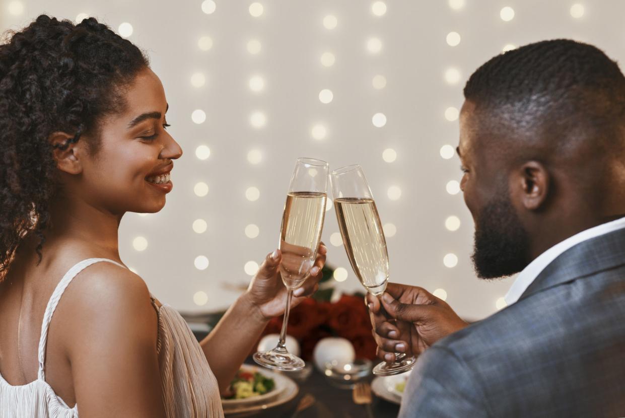 Back view of black young cheerful couple drinking champagne in restaurant, celebrating Valentine Day