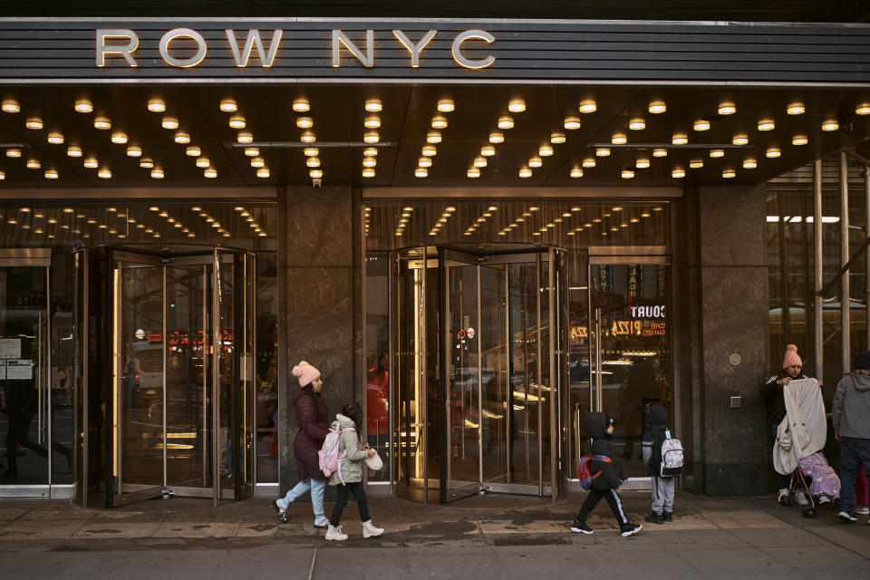 A migrant walks her child to school in front of the Row Hotel that serves as migrant shelter on Tuesday, Dec. 12, 2023, in New York. It could be a cold, grim New Year for thousands of migrant families living in New York City’s emergency shelter system. With winter setting in, they are being told they need to clear out, with no guarantee they’ll be given a bed elsewhere. (AP Photo/Andres Kudacki)