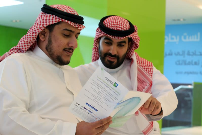 Saudi men check the prospectus of Aramco IPO, in Riyadh