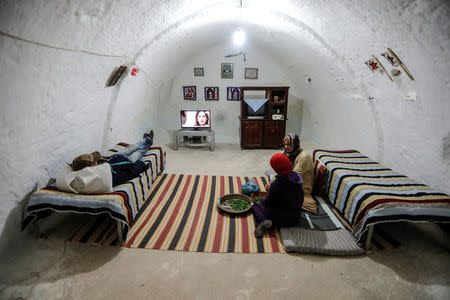 Samar, 18, and Latifa Ben Yahia, 38, (C) shell peas as their brother watches television at their troglodyte house on the outskirts of Matmata, Tunisia, February 3, 2018. REUTERS/Zohra Bensemra