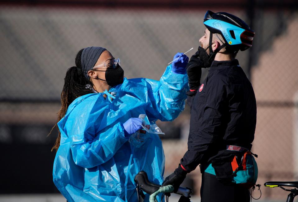 A medical technician performs a nasal swab test on a cyclist queued up in a line with motorists at a COVID-19 testing site near All City Stadium on Thursday, Dec. 30, 2021, in southeast Denver. With the rapid spread of the omicron variant paired with the Christmas holiday, testing sites have been strained to meet demand both in Colorado as well as across the country.